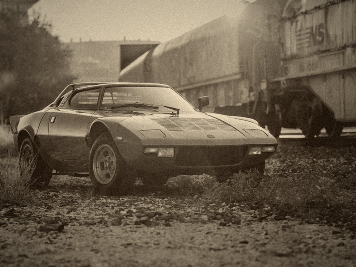 Lancia Stratos orange, vue de trois-quarts avant, devant des wagons de train au coucher du soleil